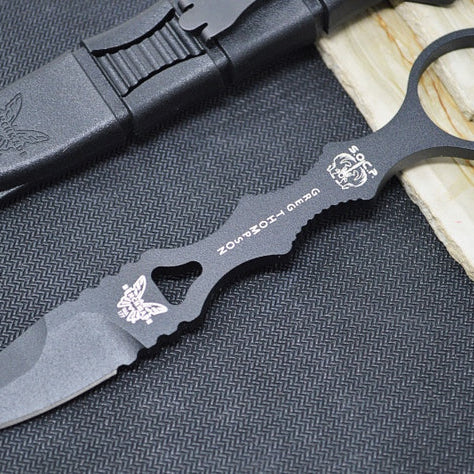 An image featuring the Benchmade 177BK SOCP dagger, which has a black combat fixed spear point blade and molded plastic handle. The dagger is displayed on a black and wood surface. Next to it is the accompanying sheath.