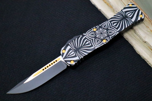 Microtech Hera "Source" Signature Series OTF - Single Edge Style / Two-toned Black Blade with Gold Accents / Black Aluminum Handle with "Source" Artwork 703-TSOS